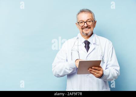 Medizinische leitender Arzt mit einem Stethoskop. Auf einem blauen Hintergrund. Ein medic hält eine Tablette in der Hand und macht einen Termin mit der Klinik. Krankheit Stockfoto