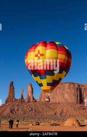 Ein Heißluftballon fliegt über einen traditionellen Hogan vor den Drei Schwestern im Monument Valley Ballon Festival im Monument Valley Navajo T Stockfoto