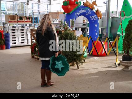 Cromwell, CT USA. Dez 2019. Frau Shopper im Freien Grasen für Weihnachtsschmuck zu einem Baumarkt, während Sie einen neuen Baum stehen. Stockfoto