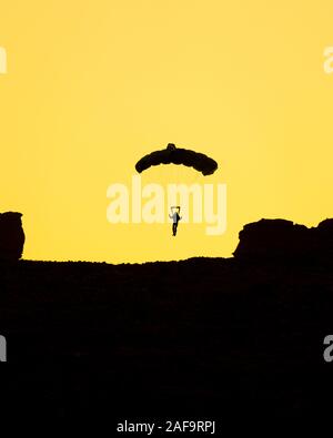 Die Silhouette einer Base Jumper Fallschirmspringen in der Kane Springs Canyon in der Nähe von Moab, Utah bei Sonnenuntergang. Stockfoto