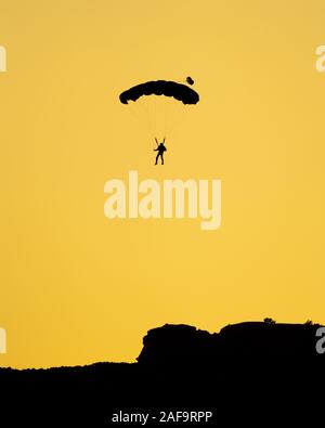 Die Silhouette einer Base Jumper Fallschirmspringen in der Kane Springs Canyon in der Nähe von Moab, Utah bei Sonnenuntergang. Stockfoto