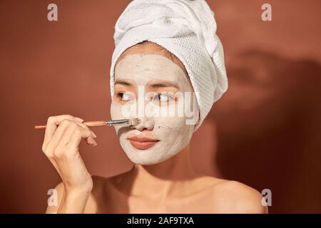 Attracitve junge asiatische Frau Anwendung Clay Mask auf Ihrem facee. Spa und Wellness, Hautpflege Produkt Konzept. Stockfoto