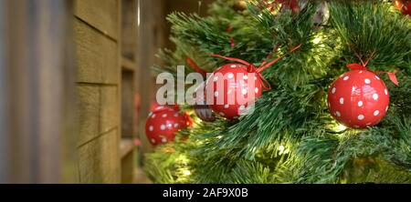 Schönen Weihnachtsbaum mit hängenden roten Kugeln und Ornamente in einem rustikalen Holzhaus Stockfoto