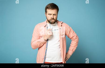 Verdächtige bärtiger Mann Brille hält an seinen Mund und schaut weg nachdenklich. Auf einem blauen Hintergrund. Stockfoto