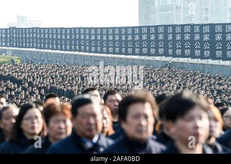 (191214) - Peking, Dez. 14, 2019 (Xinhua) - Foto am Dez. 13, 2019 zeigt die nationalen Gedenkfeier für die Opfer der Nanjing Massaker an der Memorial Hall der Opfer des Massakers von Nanjing durch die Japanischen Invasoren in Nanjing, der Hauptstadt der Provinz Jiangsu im Osten Chinas. Vor der Masse in Schwarz, Chinas nationale Flagge flog auf Halbmast als die Nation einer Trauerfeier Freitag statt der 300.000 Opfer des Massakers von Nanjing zu trauern. Fixieren eine weiße Blume, mehr als 8.000 Menschen aus allen Gesellschaftsschichten der Sechsten nationalen Trauerfeier nahmen in Nanjing, Osten Chinas Jiangs Stockfoto