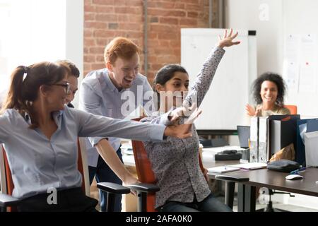 Diverse Arbeiter feiern große Nachrichten Reiten auf Bürostühle Stockfoto