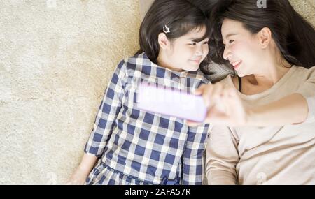 Mutter ist selfie mit ihrer kleinen Tochter mit einem smart phone Kamera während der Augenkontakt mit Tochter. asiatische Familie Konzept Stockfoto