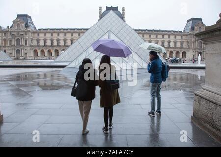 Touristen, die sich in der regen, am frühen Morgen außerhalb des Louvre und seine berühmten glaspyramide Eingang in Paris Stockfoto