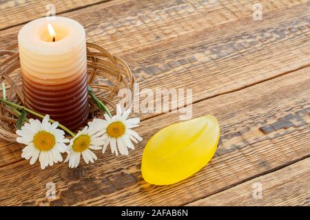 Blumenstrauß aus Gänseblümchen und brennende Kerze im Weidenkorb mit Seife auf Holzplatten. Ansicht von oben. Stockfoto