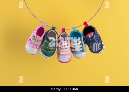 Baby Schuhe hängen auf der Wäscheleine auf gelbem Hintergrund Stockfoto