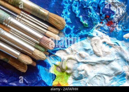 Alte gebrauchte Pinsel mit Holzgriffen auf Palette mit acryllic Farbe in verschiedenen Farben und Kopie Raum Stockfoto