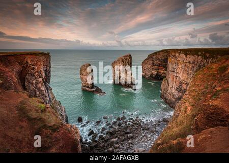 Stack rocks fotografiert bei Sonnenaufgang auf dramatische Küste von Pembrokeshire, South Wales, UK. Moody, farbenfrohen Himmel über der Bucht mit türkisfarbenem Wasser. Küste. Stockfoto