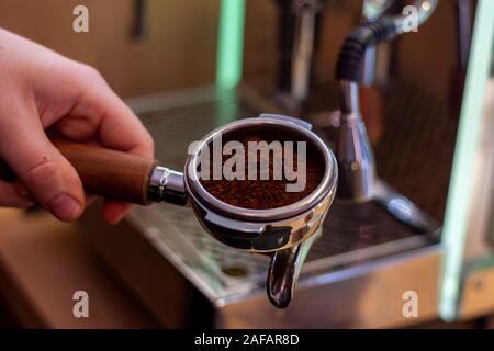 Ein Portrait eines barista Holding einen Kaffee portafilter mit frischen Kaffeesatz in es bereit einige Kaffee in der Kaffeemaschine zu machen. Stockfoto