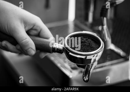 Ein Schwarz-Weiß-Porträt einer barista Holding einen Kaffee portafilter mit frischen Kaffeesatz in es bereit einige Kaffee in der Kaffeemaschine zu machen. Stockfoto