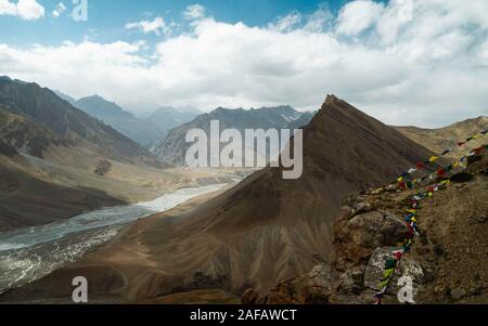 Spiti Spiti Fluss schlängelt sich durch das Tal, das von den hohen Gipfeln des Himalaya und Buddhistische Gebetsfahnen in der Nähe von Kaza, Himachal Pradesh, Indien flankiert. Stockfoto