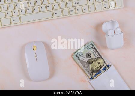 Bürobedarf, Geräte mit wireless Ladeschale, Kopfhörer, Tastatur und Maus, Bargeld von einhundert Dollar auf dem Tisch Stapel Stockfoto