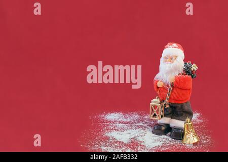 Weihnachtsmann Abbildung holding Laterne in seiner Hand auf rotem Hintergrund isoliert. Künstliche weiß Schnee und Golden Bell auf dem Boden in der Nähe von Santa. Stockfoto