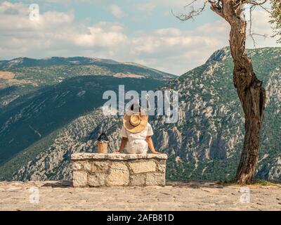 Junge Frau in Mode Kleid auf Stein becnch vor Delfi Berglandschaft in Delphi, Griechenland sitzen Stockfoto