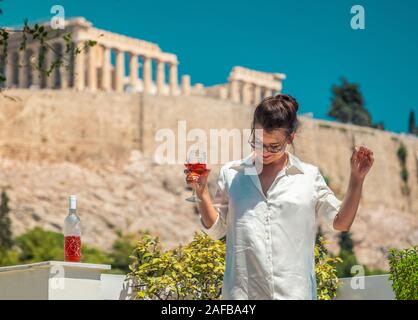 Junge Frau Tourist mit einem Drink auf Haus Balkon, mit Blick auf den Parthenon in Athen Akropolis, Griechenland Stockfoto