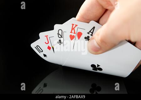 Mann hält Karten auf Schwarzer Tisch mit Reflexion. So spielen Sie "Poker, Glücksspiel im Casino Konzept. Stockfoto