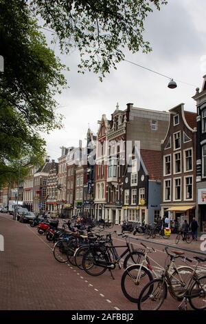 Blick auf Menschen zu Fuß auf der Amstel Straße, viele Fahrräder, historischen und traditionellen Gebäuden in Amsterdam geparkt. Es ist ein Sommertag mit bewölktem Himmel. Stockfoto