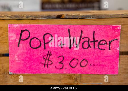 Eine bunte rosa Zeichen ist in der Nähe gesehen, eine Holzkiste, Werbung Pop und Wasser zum Verkauf auf einen Markt festen Stall in einem örtlichen Bauern fair Stockfoto