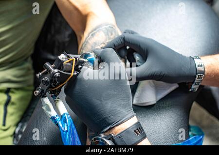 Tattoo artist in schwarz Handschuhe zieht neue Schwarz Tattoo Tattoo Maschine auf die männliche Arm des Kunden. Tattoo Salon. Stockfoto