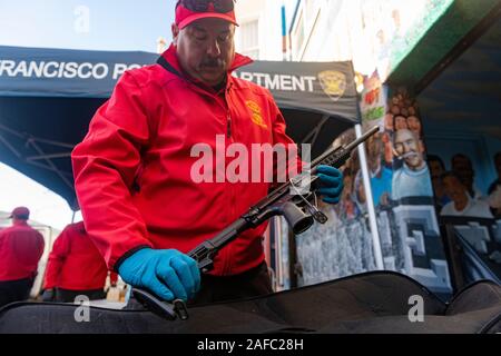 San Francisco, Ca, USA. 14 Dez, 2019. Ein San Francisco Police Officer ist Kontrolle ein AR-15 style Gewehr in von Menschen gehandelt während der jährlichen Gewehr kaufen - Zurück Veranstaltung von United Playaz in San Francisco, Kalifornien, USA am Dezember 14, 2019 gehostet wird. Heute ist der 7. Jahrestag der Sandy Hook Massenerschießungen. Credit: Sipa USA/Alamy leben Nachrichten Stockfoto