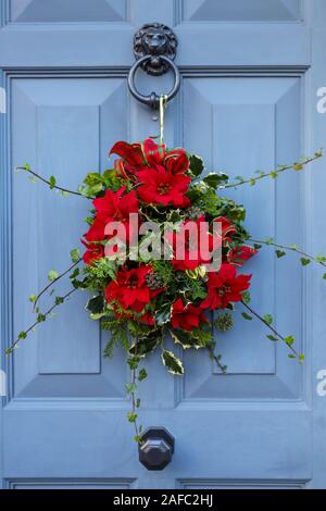 Traditionelle Festtage Weihnachten Kranz mit roten Blumen und grüne Blätter hängen in einem grauen Tür an einem Haus in Surrey, England Stockfoto