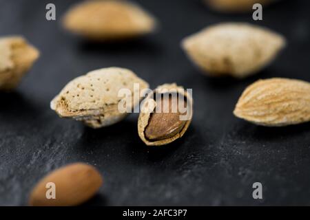 Teil der gerösteten Mandeln (in der Shell) auf dunklem Schiefer Tafel als detaillierte Nahaufnahme (selektive Fokus) Stockfoto