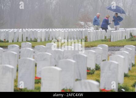 Newtown, United States. 14 Dez, 2019. Menschen gehen durch die Kränze an Grabstätten während Kränze über Amerika Samstag, 14. Dezember 2019 in Washington Crossing National Cemetery in Newtown, Pennsylvania zu legen. Tausende von Kränze werden jedes Jahr für Kränze über Amerika von Freiwilligen, die sammeln und dann die Kränze an den Gräbern der Veteranen getroffen werden. (Credit: William Thomas Kain/Alamy leben Nachrichten Stockfoto