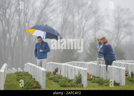 Newtown, United States. 14 Dez, 2019. Menschen gehen durch die Kränze an Grabstätten während Kränze über Amerika Samstag, 14. Dezember 2019 in Washington Crossing National Cemetery in Newtown, Pennsylvania zu legen. Tausende von Kränze werden jedes Jahr für Kränze über Amerika von Freiwilligen, die sammeln und dann die Kränze an den Gräbern der Veteranen getroffen werden. (Credit: William Thomas Kain/Alamy leben Nachrichten Stockfoto