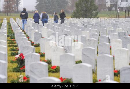 Newtown, United States. 14 Dez, 2019. Menschen gehen durch die Kränze an Grabstätten während Kränze über Amerika Samstag, 14. Dezember 2019 in Washington Crossing National Cemetery in Newtown, Pennsylvania zu legen. Tausende von Kränze werden jedes Jahr für Kränze über Amerika von Freiwilligen, die sammeln und dann die Kränze an den Gräbern der Veteranen getroffen werden. (Credit: William Thomas Kain/Alamy leben Nachrichten Stockfoto