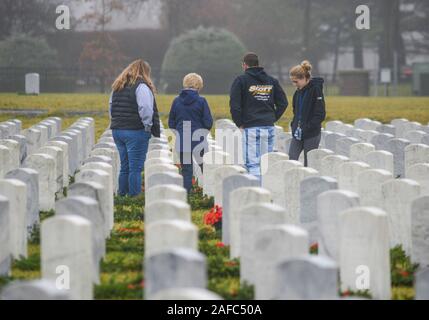 Newtown, United States. 14 Dez, 2019. Menschen gehen durch die Kränze an Grabstätten während Kränze über Amerika Samstag, 14. Dezember 2019 in Washington Crossing National Cemetery in Newtown, Pennsylvania zu legen. Tausende von Kränze werden jedes Jahr für Kränze über Amerika von Freiwilligen, die sammeln und dann die Kränze an den Gräbern der Veteranen getroffen werden. (Credit: William Thomas Kain/Alamy leben Nachrichten Stockfoto