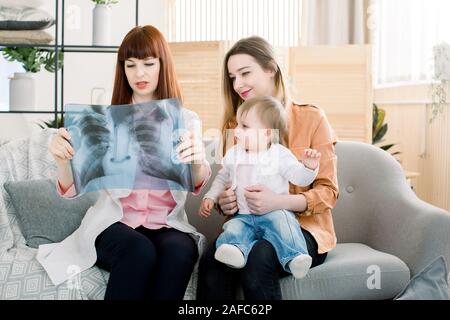 Arzt erklärt die Brust röntgen Bild Mutter mit Tochter, sitzen auf das graue Sofa in der Klinik. Stockfoto