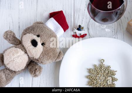 Das neue Jahr Tabelle einstellen. Spielzeug Bär in Santa's Hut, Schneeflocke, Platte und Glas mit Rotwein. Stockfoto