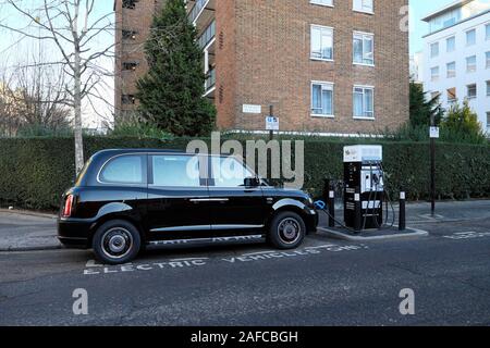 Schwarze Taxi durch eine Ladestation Betankung mit Strom in eine Straße in der City von London England UK KATHY DEWITT geparkt Stockfoto