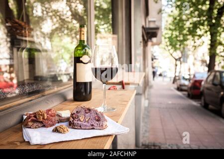 Glas und Flasche französischen Rotwein auf dem Display auf dem Tisch von der Terrasse von Paris mit Scheiben Baguette, Brie Käse und saucisson (a mich geheilt Stockfoto