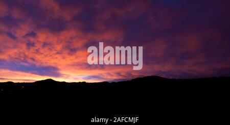 Lebendige lila und rosa Wolken bilden einen spektakulären Sonnenuntergang über dem Fernen silhouetted Berge in South Dakota. Stockfoto