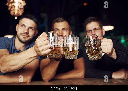 Klopfen Gläser. Drei sport Fans in einer Bar beobachten Fußball. Mit einem Bier in der Hand Stockfoto