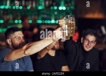 Klopfen Gläser. Drei sport Fans in einer Bar beobachten Fußball. Mit einem Bier in der Hand Stockfoto