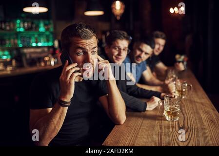 Man spricht von dem Telefon. Drei sport Fans in einer Bar beobachten Fußball. Mit einem Bier in der Hand Stockfoto