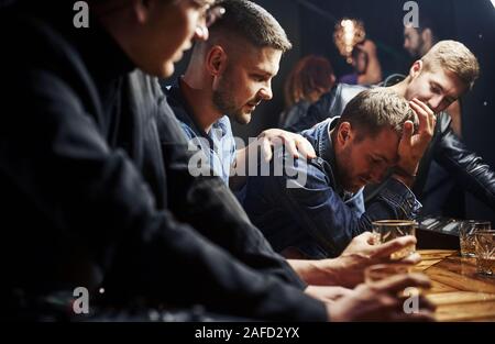 Mann fühlt sich schrecklich. Freunde in der Kneipe mit Alkohol ruht in den Händen. In Gespräch Stockfoto