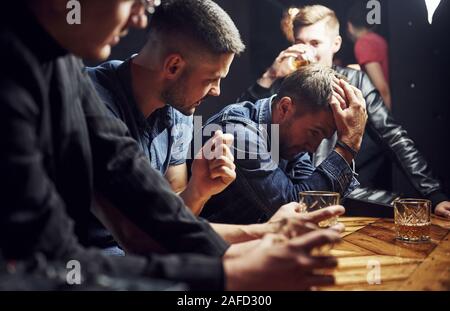 Mann fühlt sich schrecklich. Freunde in der Kneipe mit Alkohol ruht in den Händen. In Gespräch Stockfoto