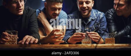 Vorderansicht. Freunde in der Kneipe mit Alkohol ruht in den Händen. In Gespräch Stockfoto