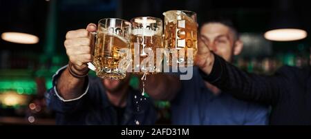 Klopfen Gläser. Drei sport Fans in einer Bar beobachten Fußball. Mit einem Bier in der Hand Stockfoto