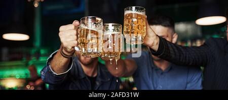 Klopfen Gläser. Drei sport Fans in einer Bar beobachten Fußball. Mit einem Bier in der Hand Stockfoto