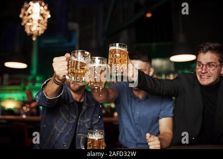 Klopfen Gläser. Drei sport Fans in einer Bar beobachten Fußball. Mit einem Bier in der Hand Stockfoto