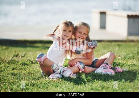 Kinder umarmen beim Sitzen auf der Wiese im Park. In Rollschuhen Stockfoto