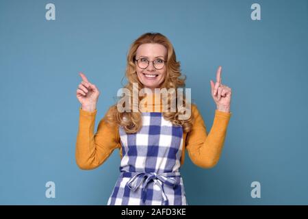 Frau mit Schürze lächelnd und mit Blick auf die Kamera zeigte mit zwei Händen Stockfoto